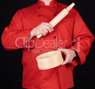 cook in a red uniform holding a wooden rolling pin and round sie
