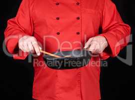 cook in red uniform holding an empty black frying pan
