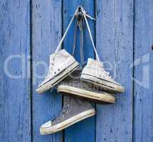 two pairs of old worn textile sneakers hang on a nail