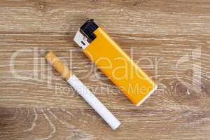 Cigarette and orange lighter on a wooden background