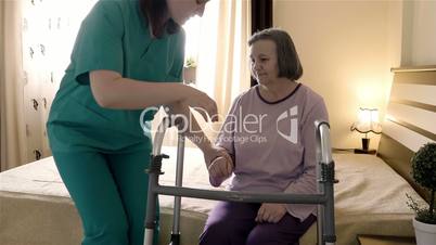 Caregiver helping senior woman getting up and walk with a walker