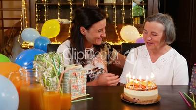 Daughter and senior mother blowing candles on birthday cake or Mothers Day party