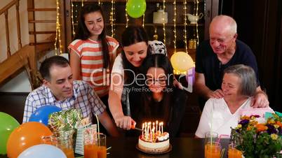 Teenage girl blowing candles on birthday cake at family party