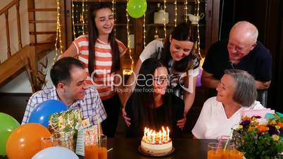 Teenage girl blowing candles on birthday cake at family party