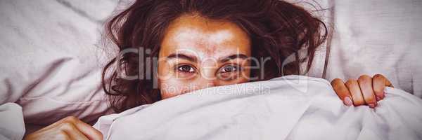 Woman hiding under blanket on bed