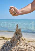 hand builds a castle from the wet sea sand