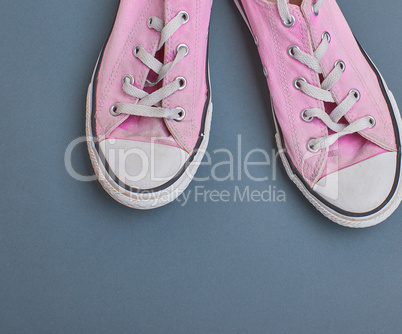 pair of old worn pink  sneakers with white laces on a black  bac