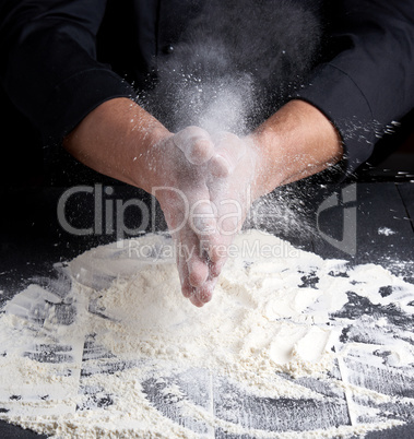 chef in black uniform pours white wheat flour out of his hands o