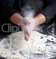 chef in black uniform pours white wheat flour out of his hands o