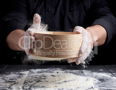 man sifts white wheat flour through a wooden sieve