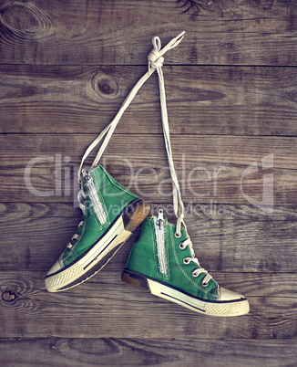 pair of old green textile sneakers hang from laces