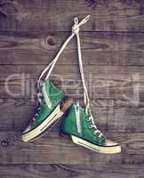 pair of old green textile sneakers hang from laces