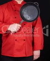 cook in red uniform holding an empty round black frying pan