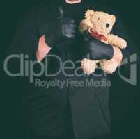 man in black clothes holding a brown teddy bear