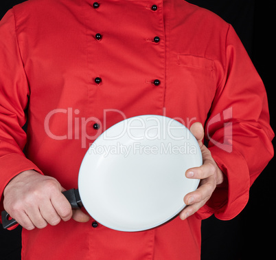 cook in red uniform holding an empty round white frying pan