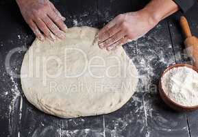 men's hands knead a round piece of dough
