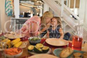 Mother whispering in daughter ear on dining table