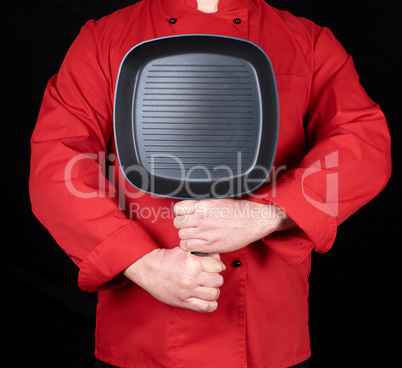 cook in red uniform holding an empty square black frying pan