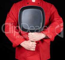cook in red uniform holding an empty square black frying pan