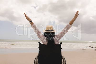 Disabled woman with arms stretched out sitting on wheelchair at beach