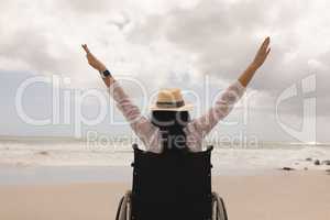 Disabled woman with arms stretched out sitting on wheelchair at beach