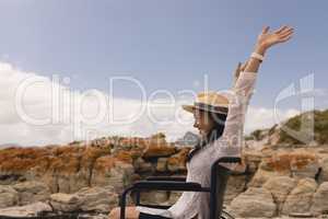 Young woman with arms up sitting on wheelchair at beach