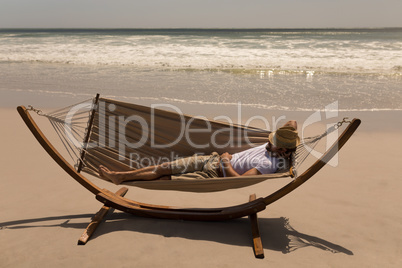 Young man with hat and hand behind hand relaxing on hammock at beach