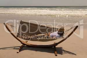 Young man with hat and hand behind hand relaxing on hammock at beach