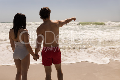Couple holding hands and man pointing at horizon on beach