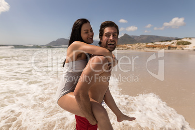 Man giving woman piggyback ride and having fun at beach