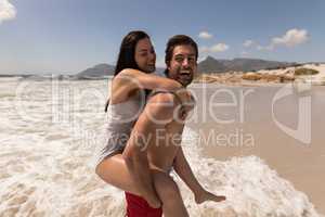 Man giving woman piggyback ride and having fun at beach