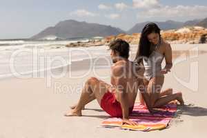 Young woman applying sunscreen lotion on mans back at beach