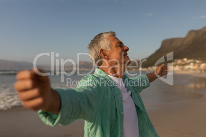 Senior man standing with arms outstretched on the beach