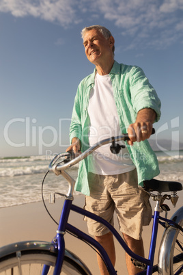 Senior man standing with bicycle on the beach