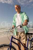 Senior man standing with bicycle on the beach