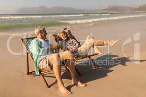 Senior couple having cocktail drink while relaxing on sun lounger at beach