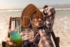Senior woman having cocktail drink while relaxing on sun lounger at beach