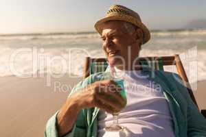 Senior man having cocktail drink while relaxing on sun lounger at beach