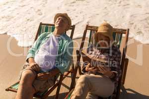 Senior woman reading a book while senior man relaxing on sun lounger at beach