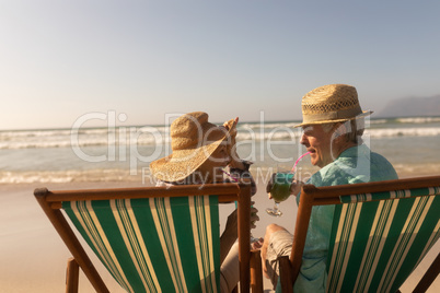 Senior couple having cocktail drink while relaxing on sun lounger at beach