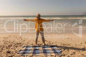 Senior woman standing with arms outstretched on the beach
