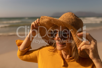 Senior woman in hat and sunglasses standing on the beach
