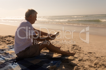 Senior man reading a book while relaxing on picnic blanket at beach