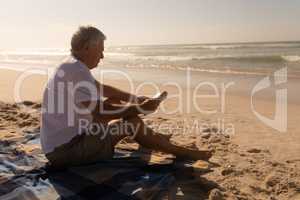 Senior man reading a book while relaxing on picnic blanket at beach