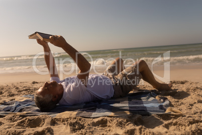 Senior man reading a book while relaxing on picnic blanket at beach