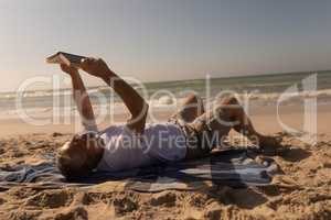 Senior man reading a book while relaxing on picnic blanket at beach