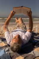 Senior man reading a book while relaxing on picnic blanket at beach