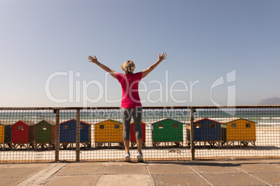 Senior woman standing with arms outstretched on a promenade at beach