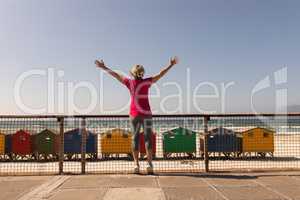Senior woman standing with arms outstretched on a promenade at beach