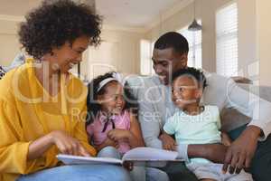 Happy African American parents with their cute children reading storybook on the sofa